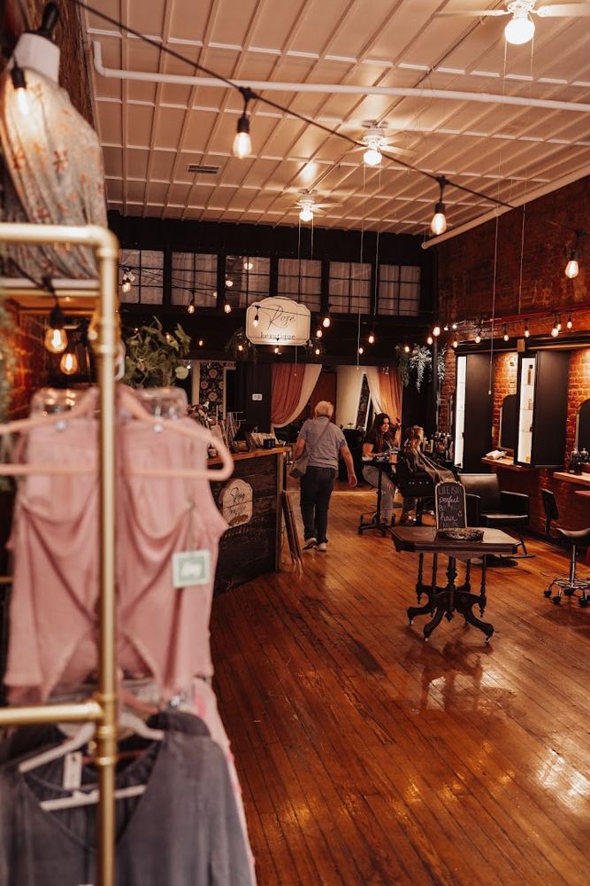 Inside Rosé Beautique: wood floors, brass clothing racks, string lights and salon chairs under a pressed-tin ceiling